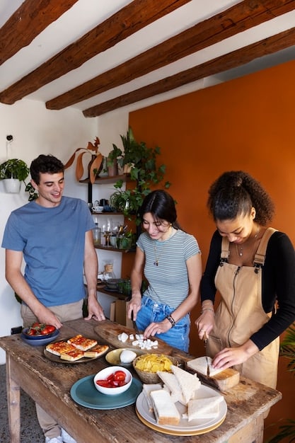 A brightly lit and inviting community kitchen scene. Volunteers are preparing meals using rescued food while wearing aprons and smiling. The kitchen is well-equipped and organized, with fresh ingredients displayed prominently. In the background, a group of people are seated at tables, enjoying the meal in a communal setting.