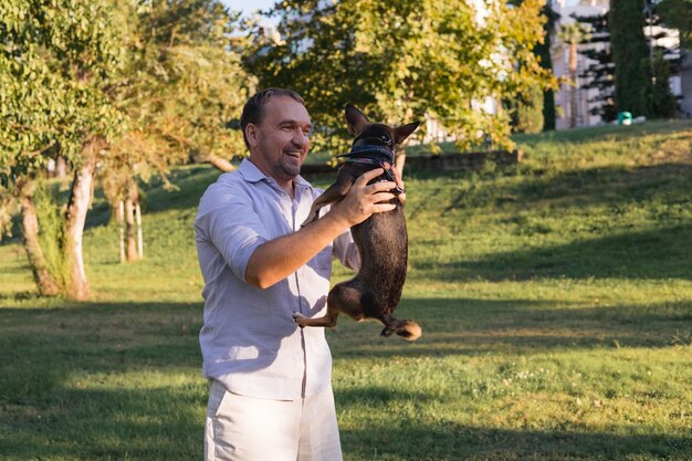 A trainer working with a German Shepherd service dog in a public park. The trainer is giving the dog a hand signal, and the dog is attentively focused on the trainer. In the background, people are walking and playing.