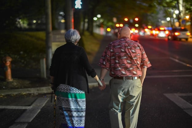A person helping an elderly individual cross a street, showcasing a direct act of kindness and assistance. The background should be a busy city intersection.