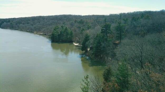 A wide shot of a pristine river flowing through a forested area in the US, with a conservation easement sign visible. The image should showcase the natural beauty of the protected land and the river's ecosystem.