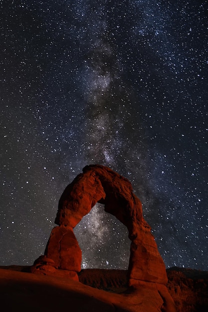 Arches National Park at night, with the Milky Way stretching over the iconic red rock arches. Stars and planets are glittering in the sky.