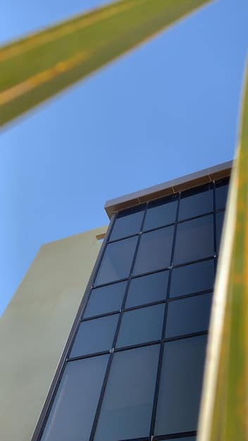 A close-up of a solar panel installation on a rooftop, showcasing the sleek design and integration with the building's architecture. The panels are dark blue and reflect the sunlight, with green trees and blue sky visible in the background.