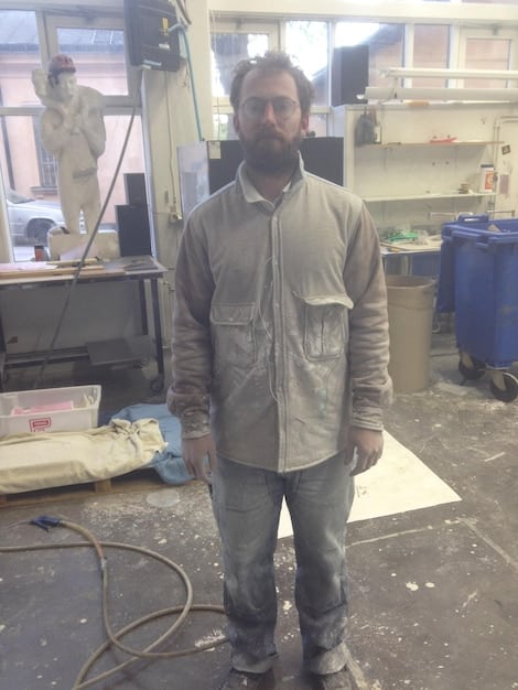 A formerly homeless individual, now employed, stands proudly in their work uniform, smiling and confident. The background shows a supportive workplace environment.