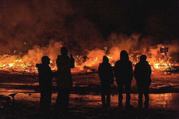 A group of firefighters standing side-by-side, looking somber but proud. They are covered in soot and water, with the blurred background showing the aftermath of the fire.