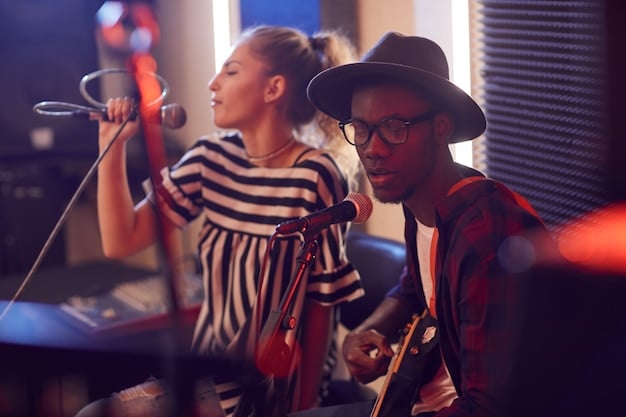 A diverse group of teenagers collaborating on a songwriting project in a modern recording studio. They are working together, using computers, instruments, and microphones, and seem deeply engaged and excited about their creative work.