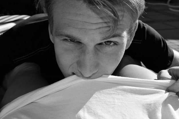 A close-up black and white photograph of the athlete's face as they lie in a hospital bed, eyes closed and a look of pain etched on their face. Medical equipment surrounds them, highlighting the severity of their injury.