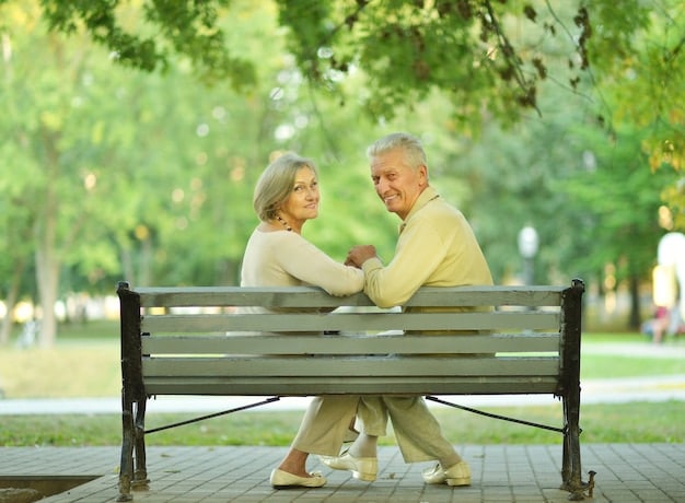 An elderly couple sits together on a park bench, engaged in conversation while looking at a tablet displaying financial data. Sunlight filters through the trees, creating a serene atmosphere, symbolizing thoughtful retirement planning. Includes visual elements and feelings of security, support, and connection in retirement.