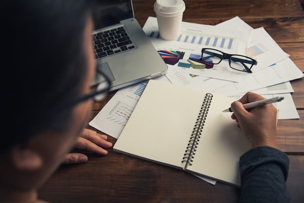 A person studying financial documents with charts and graphs, with a notebook and pen nearby. The image represents financial planning and strategic decision-making to maximize tax refunds.